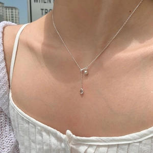 Close-up of silver chain necklace with teardrop and ball pendant on model neck