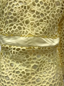 Détail d'une robe en dentelle jaune avec ceinture en satin et texture crochetée
