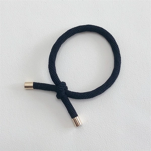Macro detail of black braided elastic hair tie with polished gold metal cylinder buckle