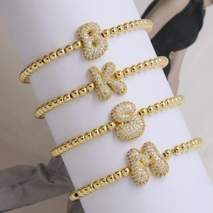 Golden bead bracelets with zircon-inlaid 18k balloon alphabet charms on white display