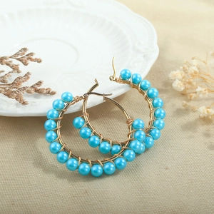 Detail of handmade gold wire hoop earrings with sky blue beads on a decorative plate