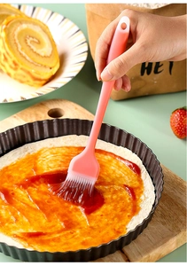 Pink silicone pastry brush spreading sauce on dough in a cozy kitchen baking setting