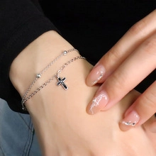 Detail of silver double-layer bracelet with small beads and a black cross pendant