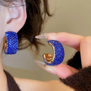 Close-up of gold C-shaped earrings with pave-set royal blue crystals for women
