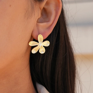 Detailed macro view of gold flower earrings with brushed metal texture and zircon center