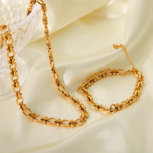 Detailed close-up of golden stainless steel necklace and bracelet set on silk background