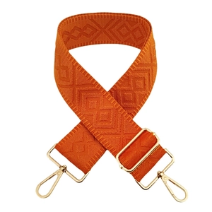 Macro shot of orange woven bag strap with textured diamond pattern and gold metal hardware