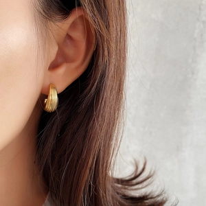 Detail of a minimalist gold textured hoop earring worn by a model in a close-up view