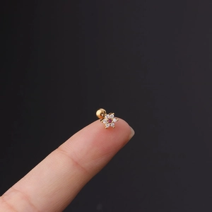 Macro shot of tiny gold floral helix stud earring with purple zircon on a fingertip