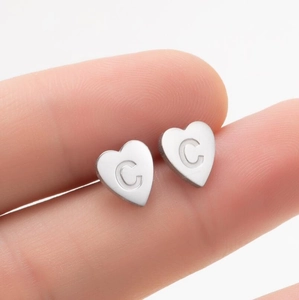 Gros plan de boucles d'oreilles cœur en acier inoxydable avec gravure C à la main