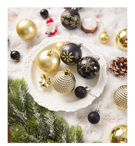 Close-up of gold and black Christmas ball ornaments and stars on white plate with snow