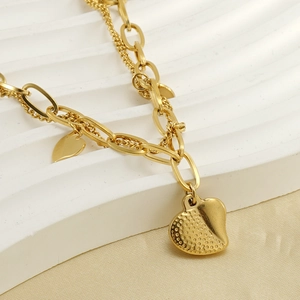Detail of gold double-layer chain bracelet with textured heart charms on silk background