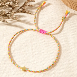 Detailed macro view of woven multi-color rope bracelet with a gold cross charm and beads