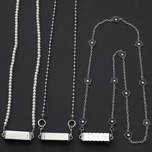 Detail of pearl bead, metal ball chain, and black flower strap with engraved charms