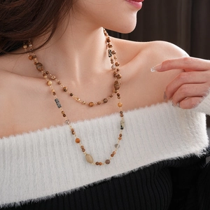 Detail of layered earthy beaded long necklace with gold chain on fashion model