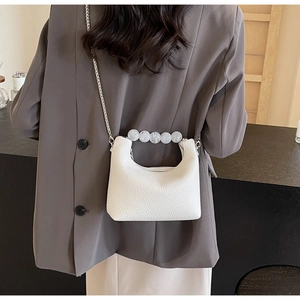 Detail of white textured mini bag with elegant pearl handle and silver chain strap