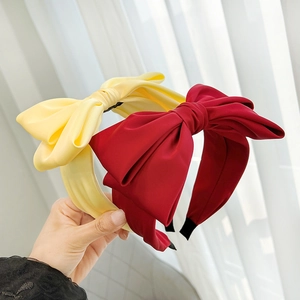 Detail of elegant yellow and red satin bow headbands held against a soft curtain