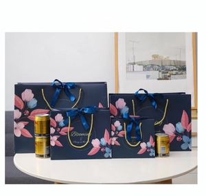 Close-up of four navy blue floral gift bags with gold handles and silk bows in various sizes