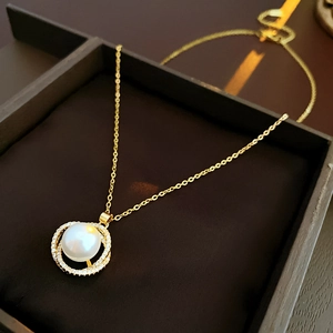 Detail eines goldenen Doppelring-Anhängers mit weißer Perle in einer dunklen Holzkiste