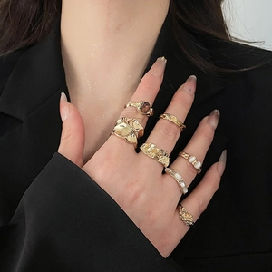 Detail showing stacked golden alloy rings with lava texture and inlaid gemstones on hand
