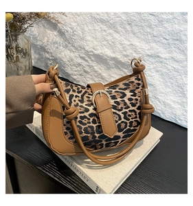 Detailed view of leopard print shoulder bag with brown leather accents on a book background