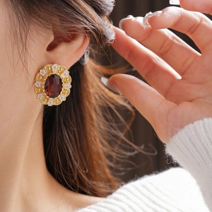 Close-up of vintage gold earring with a dark red oval gemstone and white floral motifs