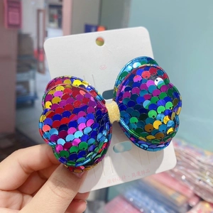 Close-up of a colorful sequined bow hair clip with iridescent finish on a card