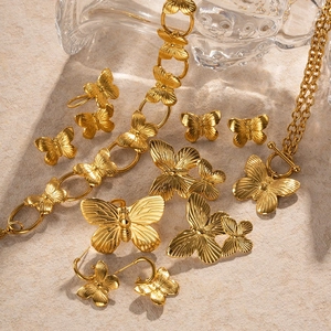 Gold plated butterfly necklace and earring jewelry set on a neutral textured background