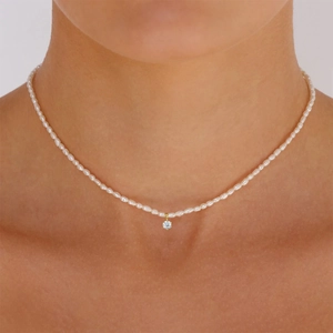 Detail of a gold-plated pearl necklace with a single diamond pendant worn by a model