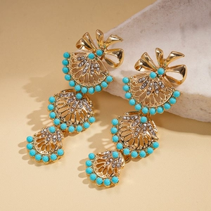 Detail view of gold fan earrings with turquoise beads and white rhinestones on marble