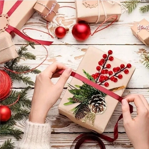 Close-up of hands decorating craft paper gift boxes with red berries and pine needles