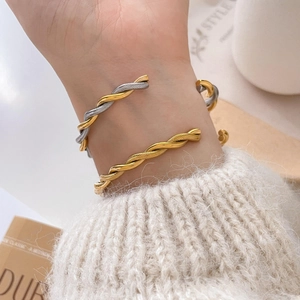 Close-up of twisted bangle bracelets in two-tone gold and silver on a knit sleeve