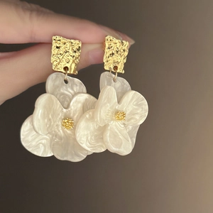 Detailed close-up of acrylic flower earrings featuring gold-tone textured metal studs