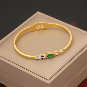Macro shot of gold snake bracelet with emerald green teardrop gem on jewelry box
