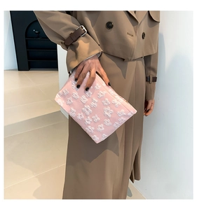 Close-up of pink clutch bag with white floral embossed patterns held by a model