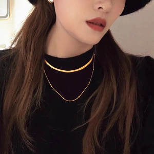 Double-layered gold snake chain and beaded necklace set worn on a black turtleneck