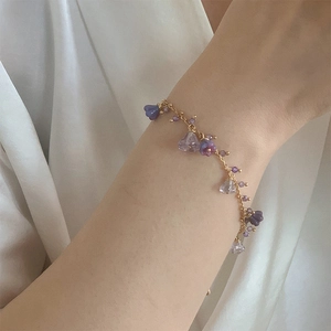 Elegant gold chain bracelet with purple crystal floral charms on a female model wrist