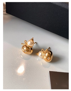 Détail de boucles d'oreilles gourde dorées avec perles blanches et cristaux étoilés