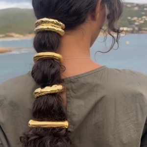 Detail of a retro gold double-layered metallic hair tie on a ponytail with a beach view