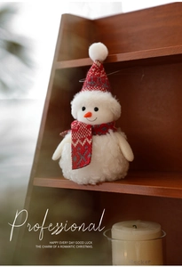 Close-up of a plush Christmas snowman with red and gray knitted hat on a wooden shelf