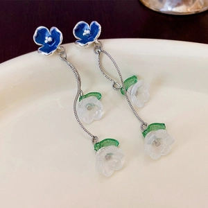Detail of blue enamel flower earrings with resin petals on a beige ceramic plate