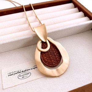 Detail of matte gold water drop pendant with dark wood texture in a luxury jewelry box