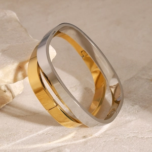 Minimalist gold and silver stainless steel clasp bracelets stacked on a light stone base