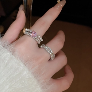 Détail de bagues argentées avec pierre cœur rose, perle blanche et zircon au doigt du modèle