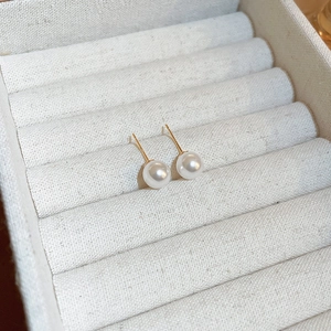 Detail view of minimalist pearl stud earrings with gold needles on white textured jewelry box