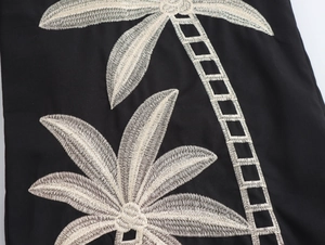 Detailaufnahme der beigefarbenen Palmenstickerei auf schwarzem Stoff der Freizeithose