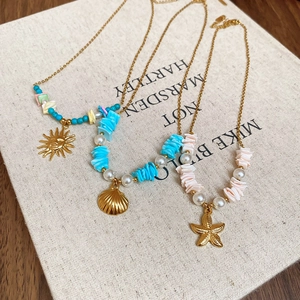 Detail of three gold ocean charm necklaces with starfish and shells on white fabric