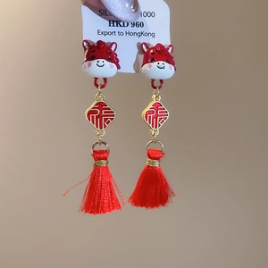 Detail of red tassel earrings featuring a golden Fu character and enamel bull motif