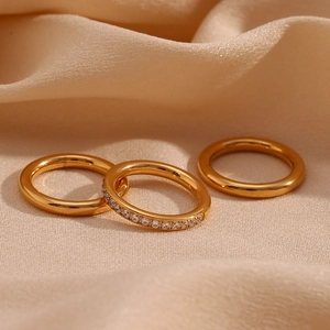 Detailed shot of three gold-plated stainless steel rings with zircon on soft beige fabric