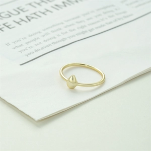 Detailed close-up of a minimalist gold teardrop ring on a white artistic paper background